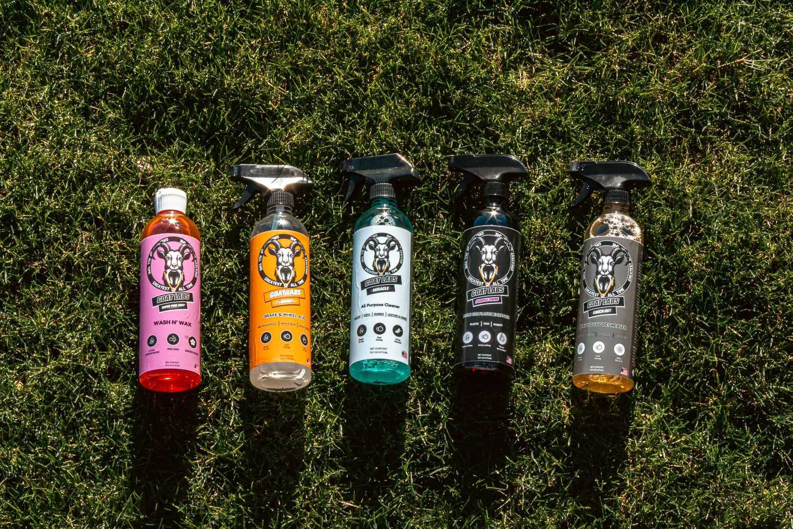 A range of car care products from Goat Lab laid out on grass, including bottles of shampoo, polish, and cleaners.